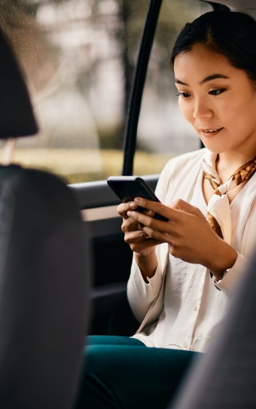 Asian female executive using smart phone while driving in a car.